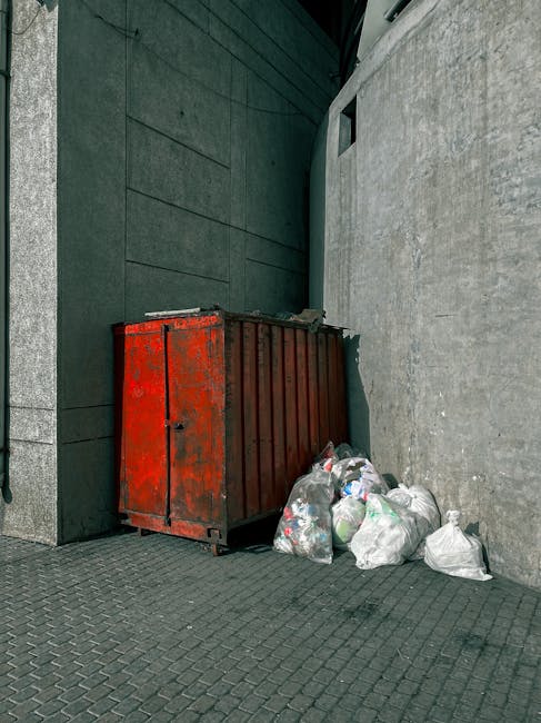 A green, old-style clothing collection bin situated outdoors, with Chinese characters and a contact phone number on the front panel. The bin features separate compartments labeled for items such as cl